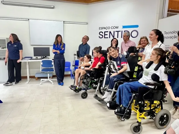 Várias pessoas, incluindo utilizadores de cadeiras de rodas, observam uma demonstração de tecnologia assistiva no interior do Espaço com Sentido.